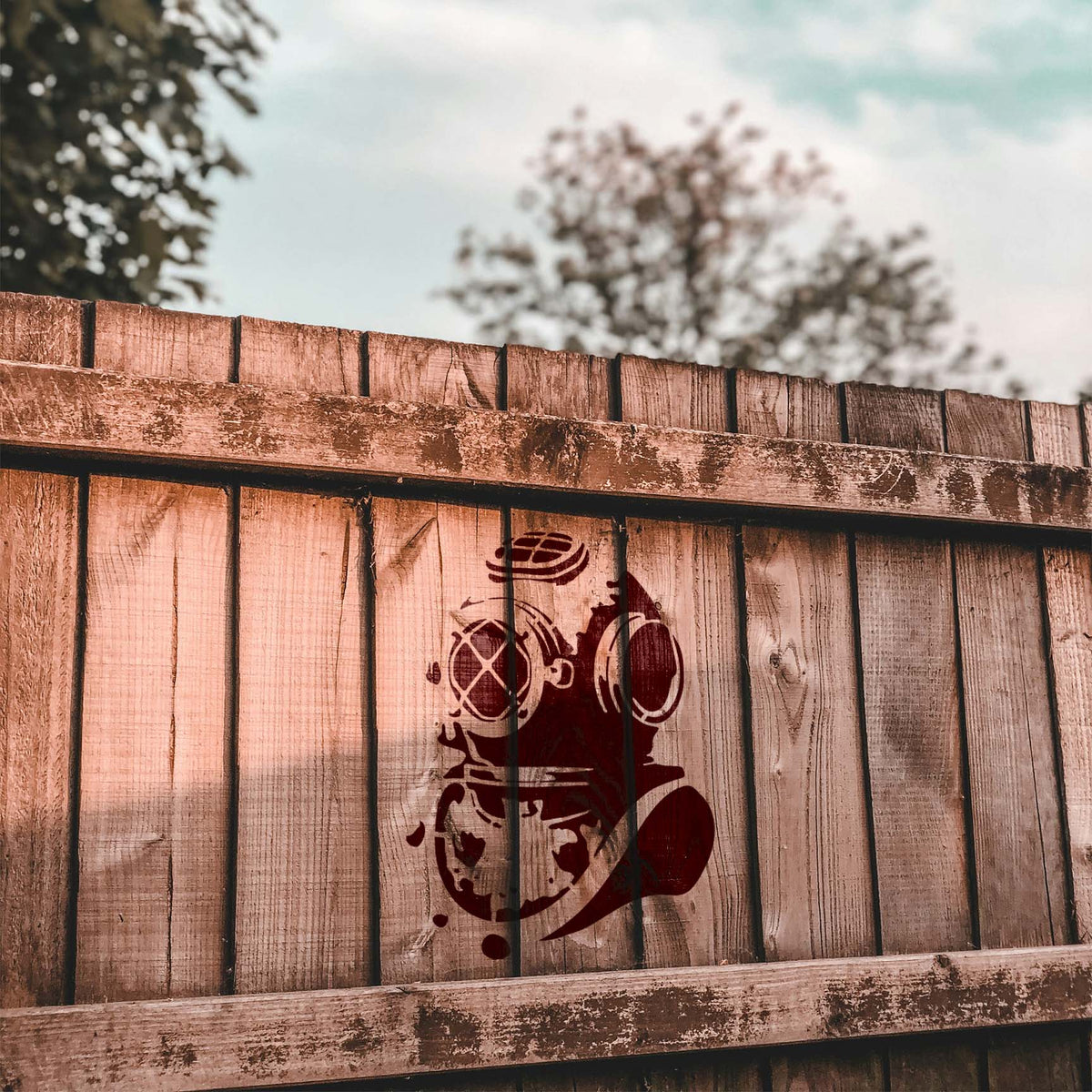Rustic wood fence displays the Deep Sea Diver Helmet Stencil painted in dark red
