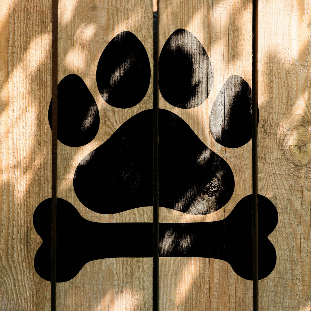 Rustic wood planks showcase the Dog Paw Print and Bone Stencil beneath dappled sunlight