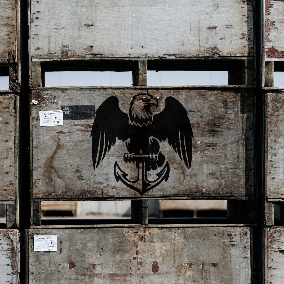 A bold Eagle and Anchor Emblem Stencil decorates weathered wooden crates with striking black nautical artwork.
