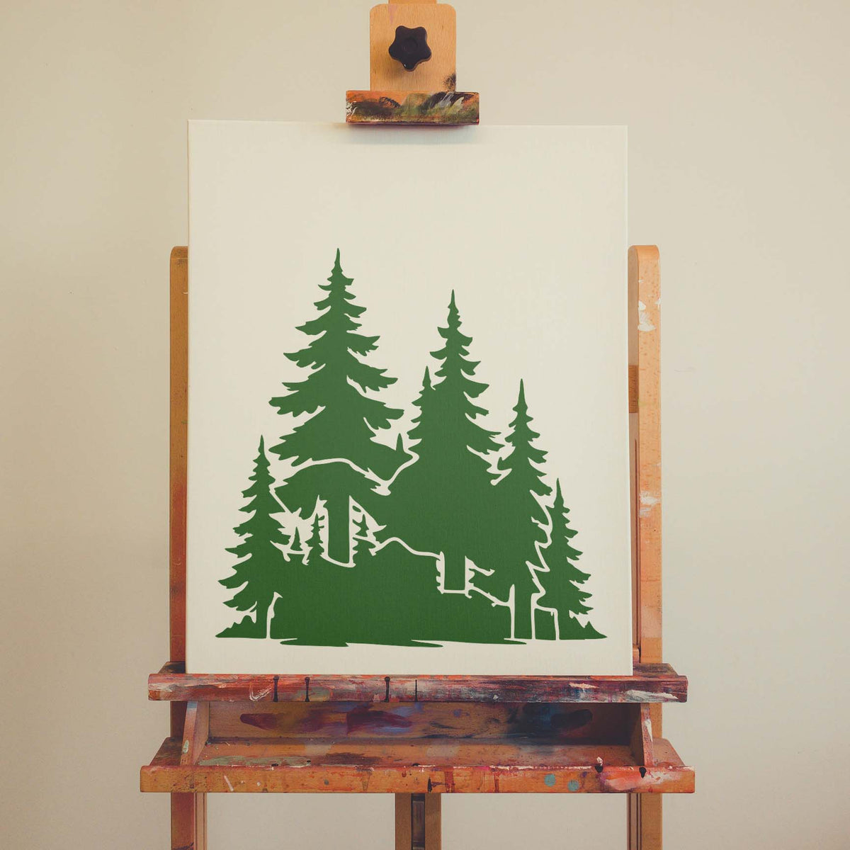 Evergreen Woodland Trees Stencil displays a cluster of green pine trees on a cream canvas resting on an easel.