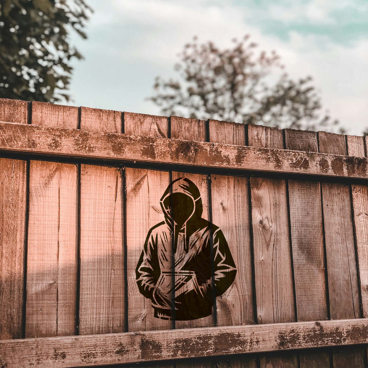 On a weathered wood fence, the Faceless Hooded Figure Stencil creates a bold street-art look.