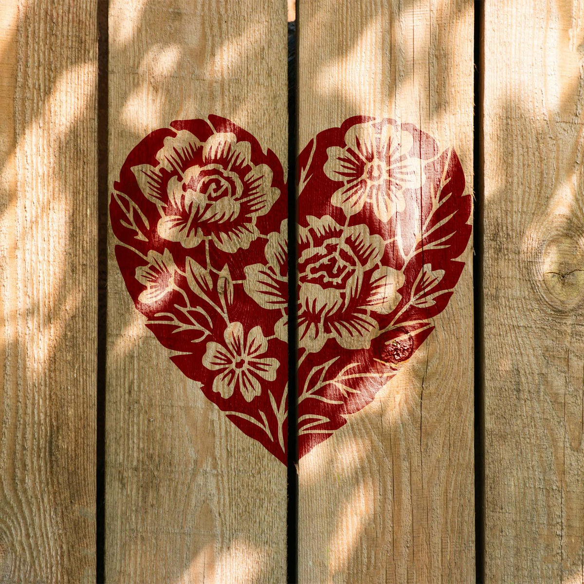 Floral Heart Bouquet Stencil shown in red on a sunlit wooden fence panel.