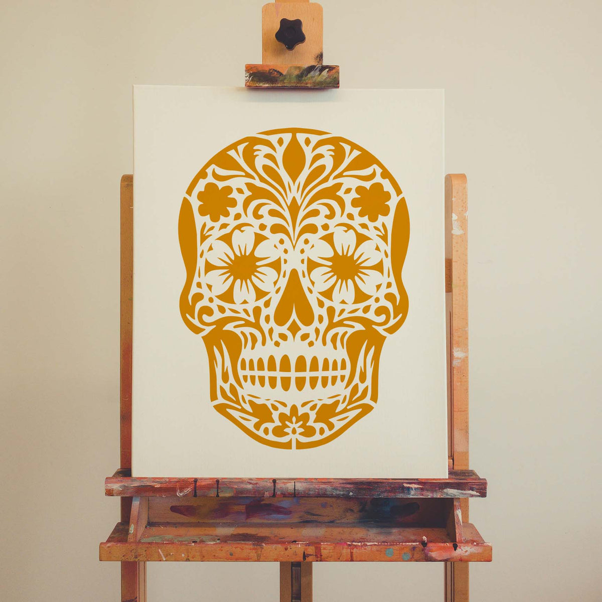 Intricate flowers fill the golden Floral Sugar Skull Stencil displayed on an artist canvas
