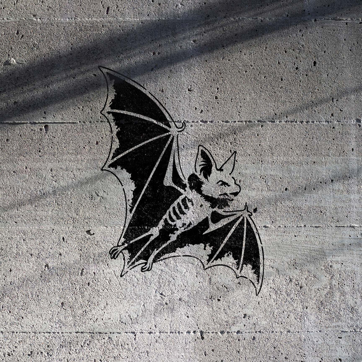 Flying Bat Stencil shown in black on a sunlit concrete wall with diagonal shadow lines.
