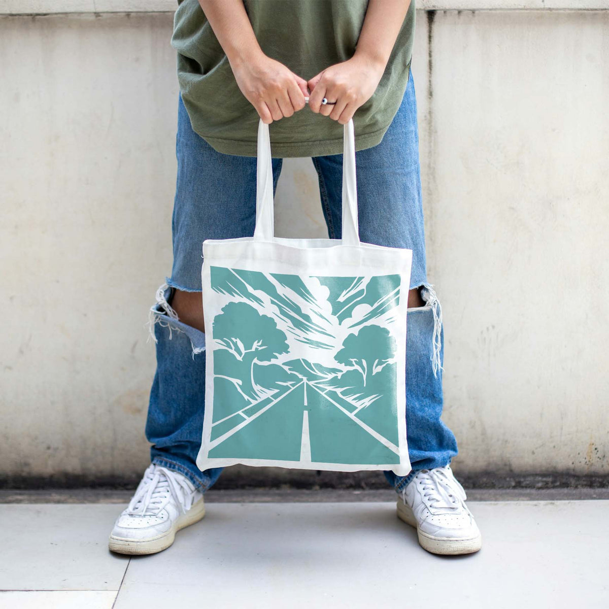 Winding into the distance, the Forest Highway Horizon Stencil decorates a white tote bag in soft teal.