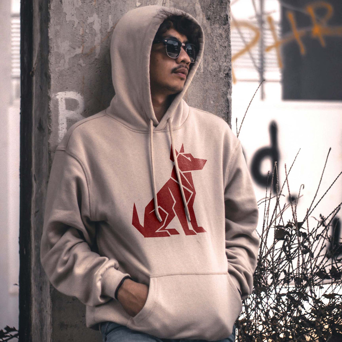 Geometric Sitting Dog Stencil printed in red on a beige hoodie in an urban portrait.