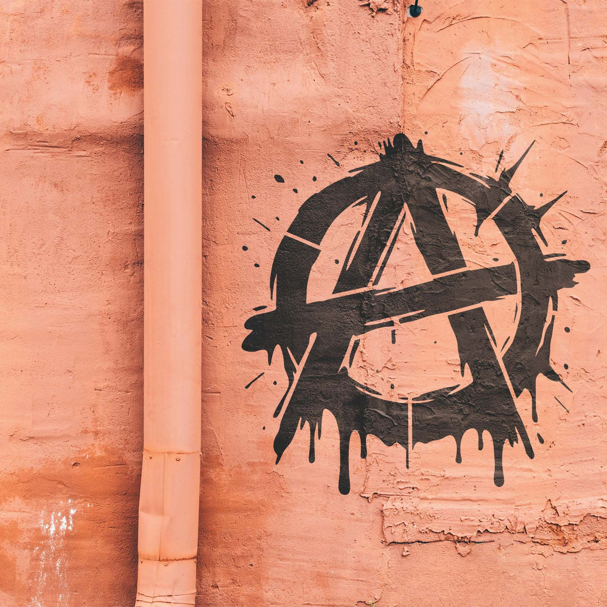 Black paint drips and sharp strokes bring the Graffiti Anarchy Symbol Stencil to life on a peach wall.