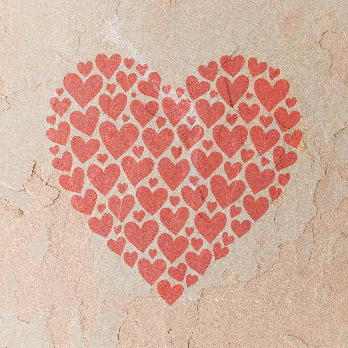 Heart Mosaic Stencil forms one large coral heart from dozens of smaller hearts on a rustic stucco wall