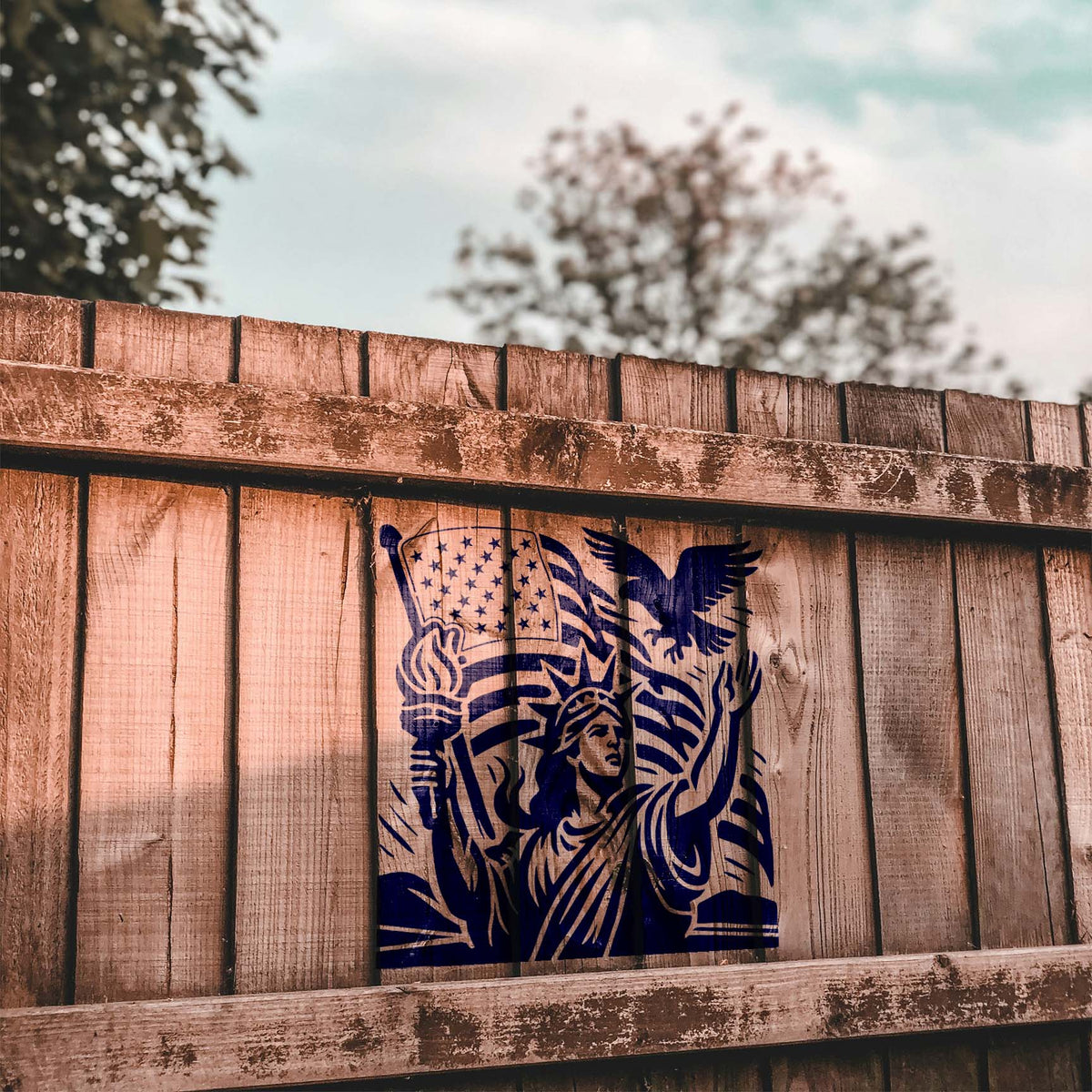 Painted on a rustic wood fence, Liberty & Freedom Patriotic Stencil shows Lady Liberty, eagle, and flag