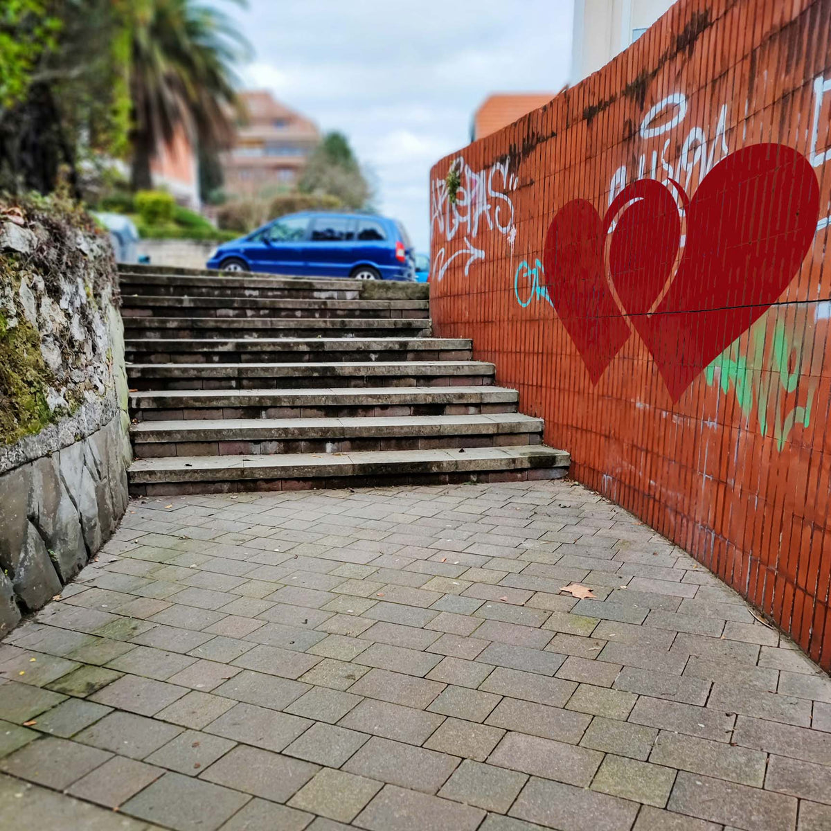 Oversized Linked Hearts Stencil appears in red on a graffiti-covered brick wall beside outdoor steps