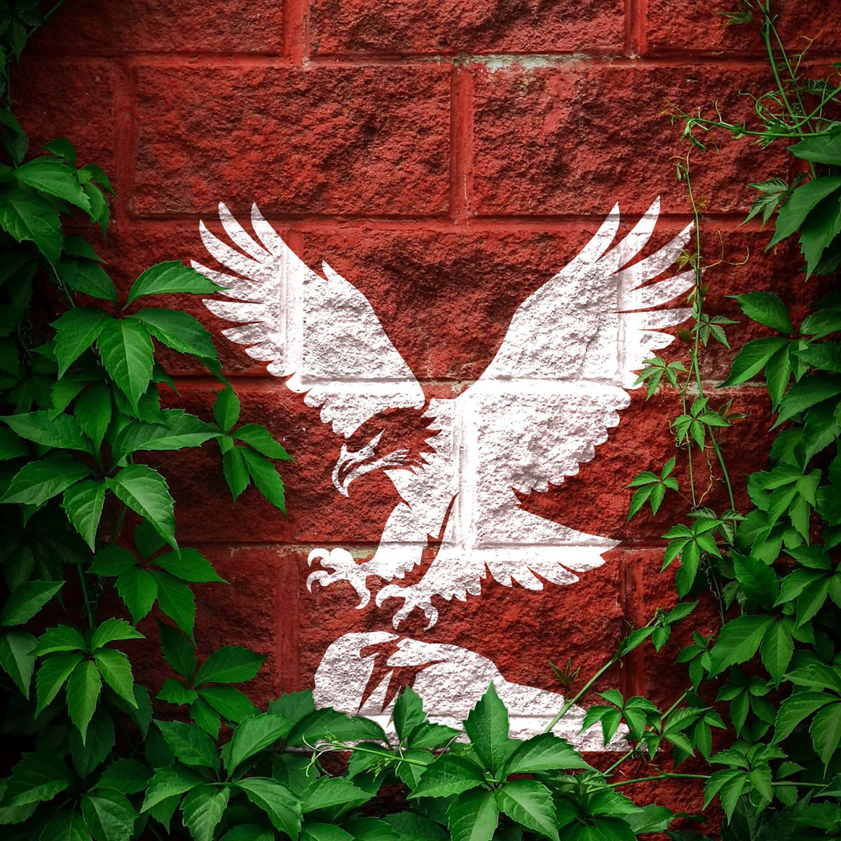 Framed by green ivy, the Majestic Eagle Landing Stencil shows a white eagle descending toward a rock.