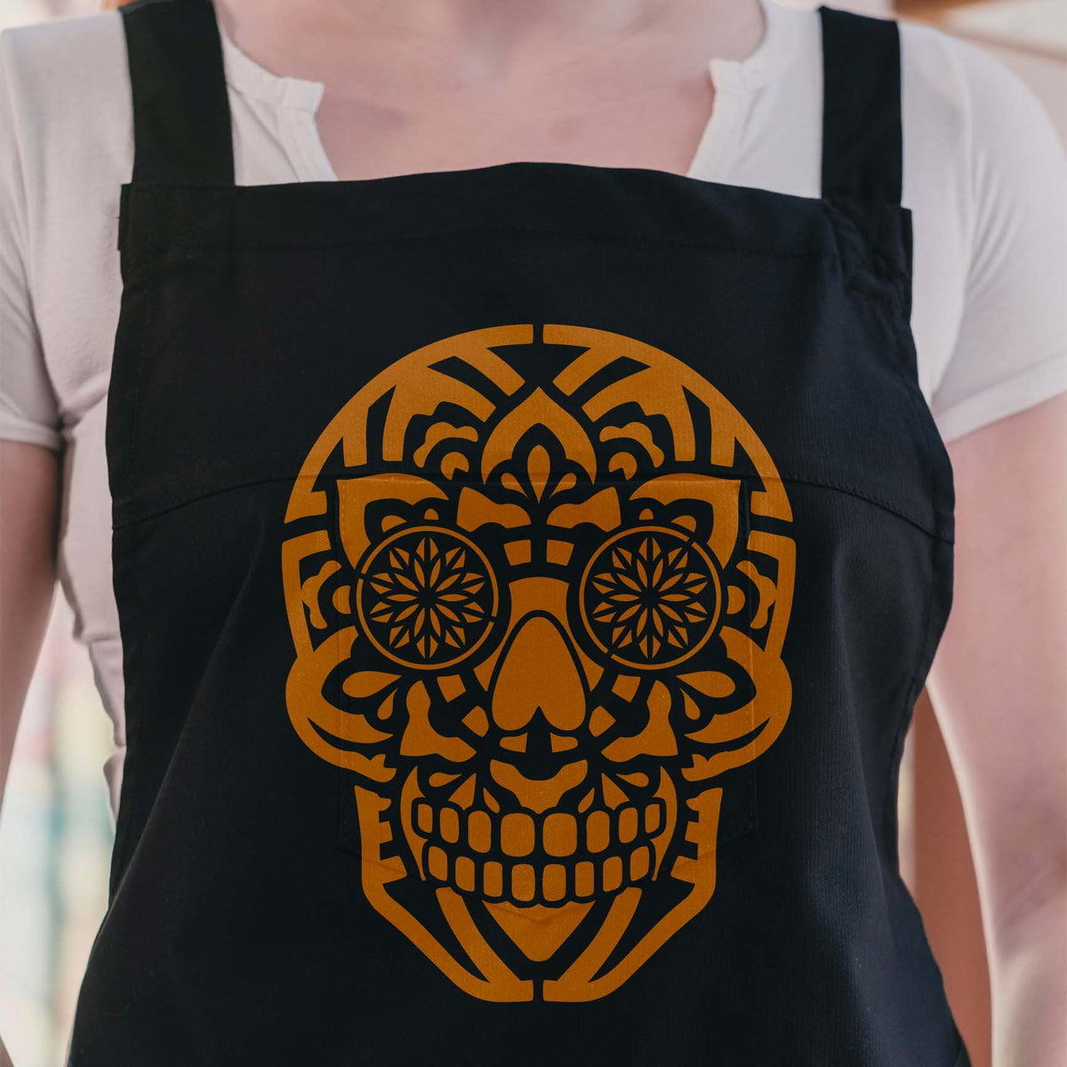 Mandala Sugar Skull Stencil in warm orange adds intricate detail to a black apron