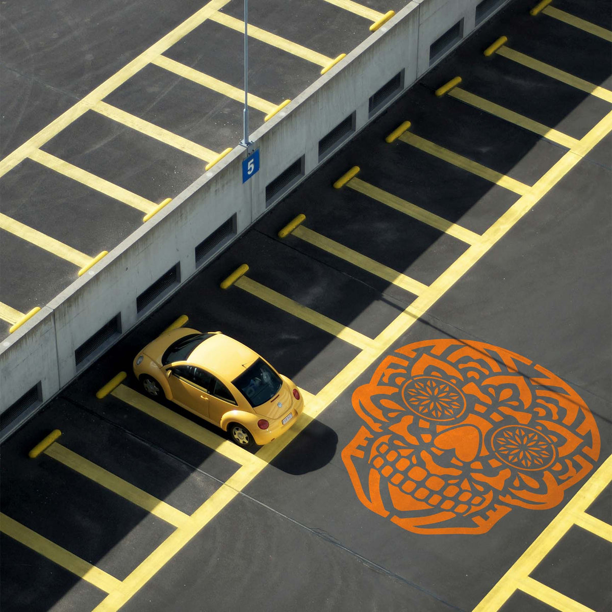 Oversized orange Mandala Sugar Skull Stencil decorates the pavement of a parking lot