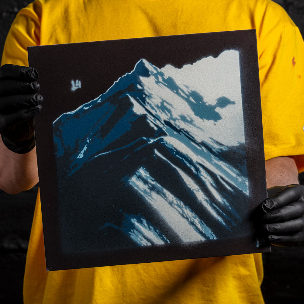 Mountain peak layered stencil artwork in blue and white spray paint held by artist wearing black gloves