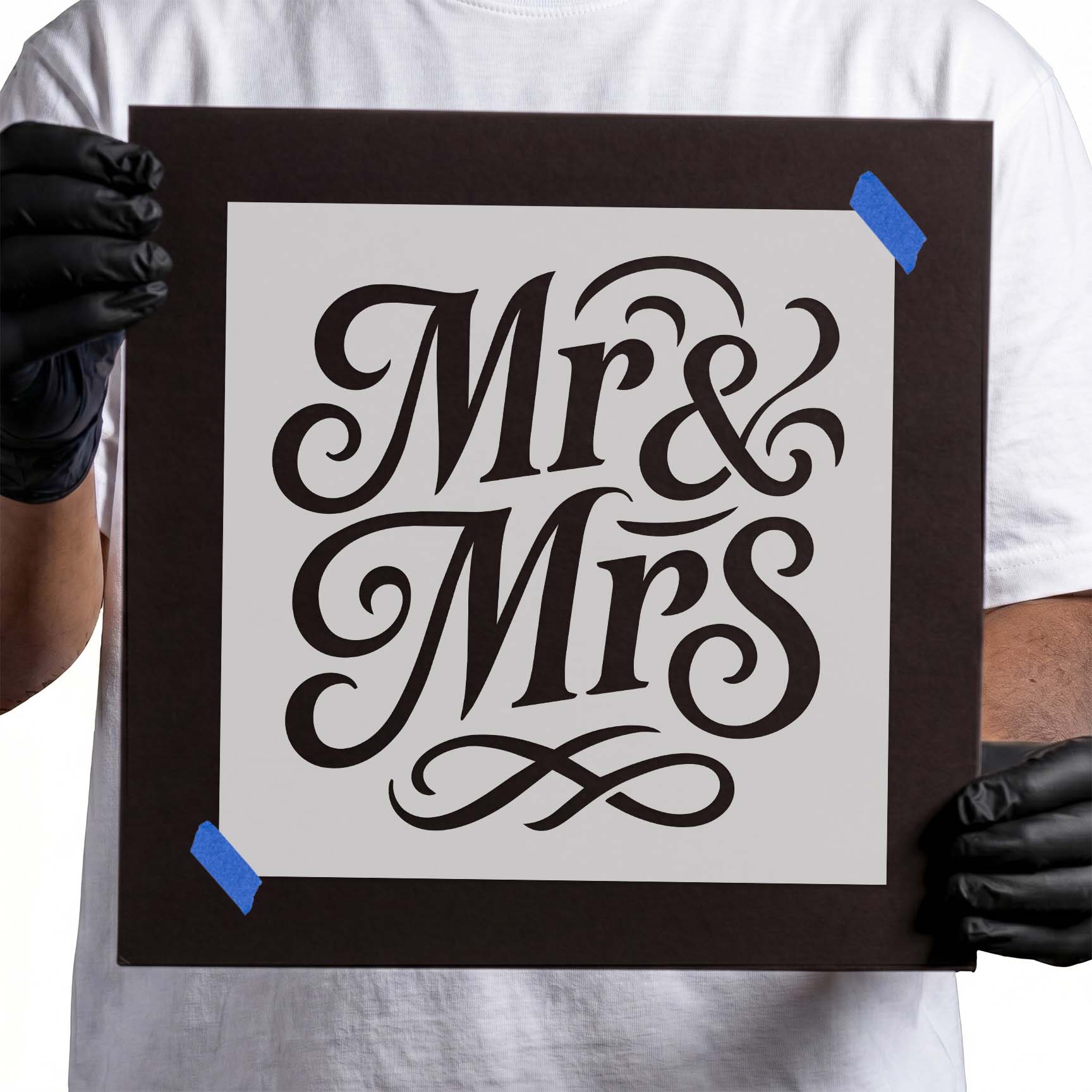 Gloved hands holding Elegant Mr & Mrs Script Stencil taped to cardboard