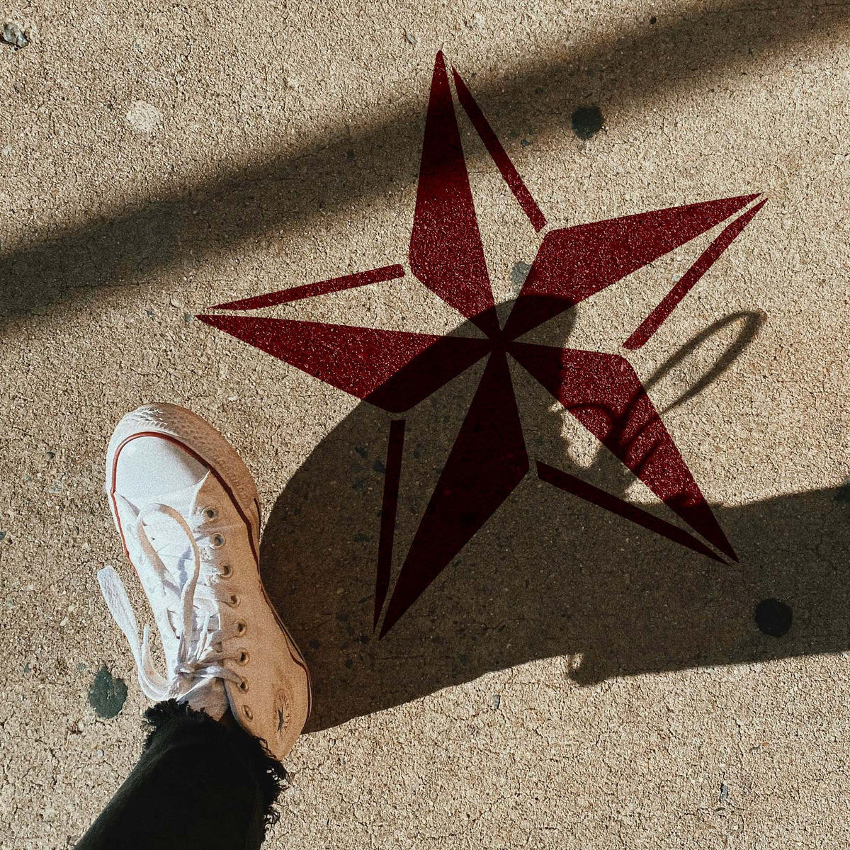 Nautical Star Stencil painted red on concrete beside a white sneaker