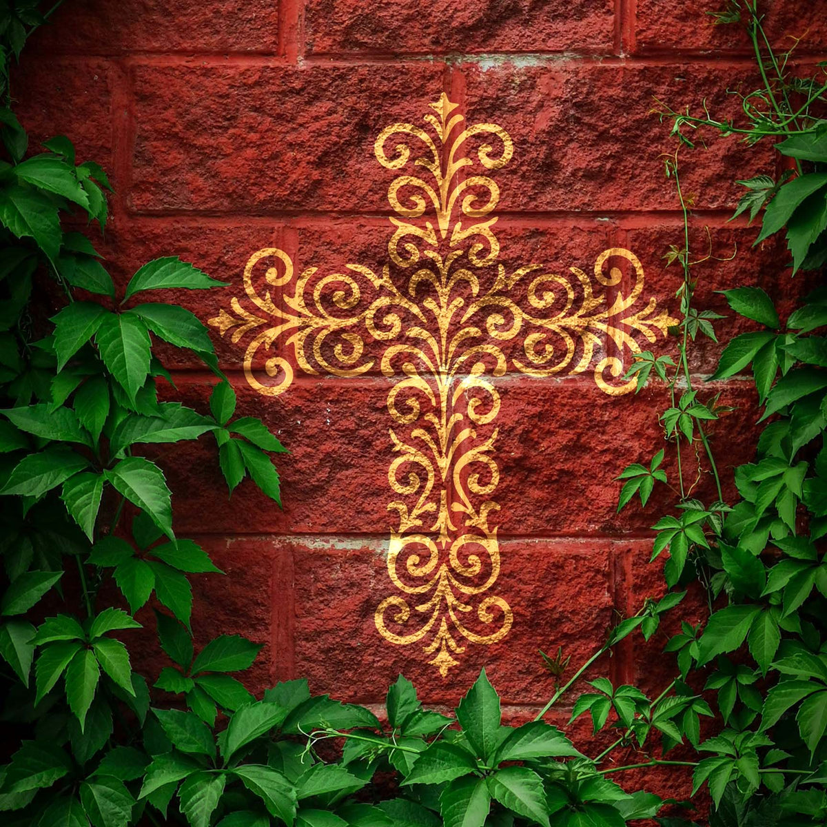 Golden Ornate Filigree Cross Stencil shines against a rustic red brick wall surrounded by green vines