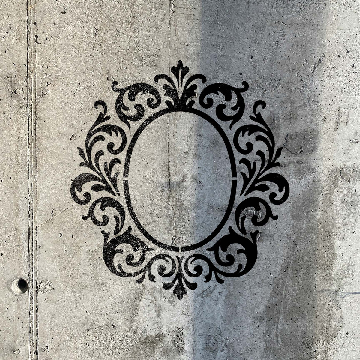 Weathered concrete showcases the Ornate Monogram Frame Stencil with sweeping floral scrollwork
