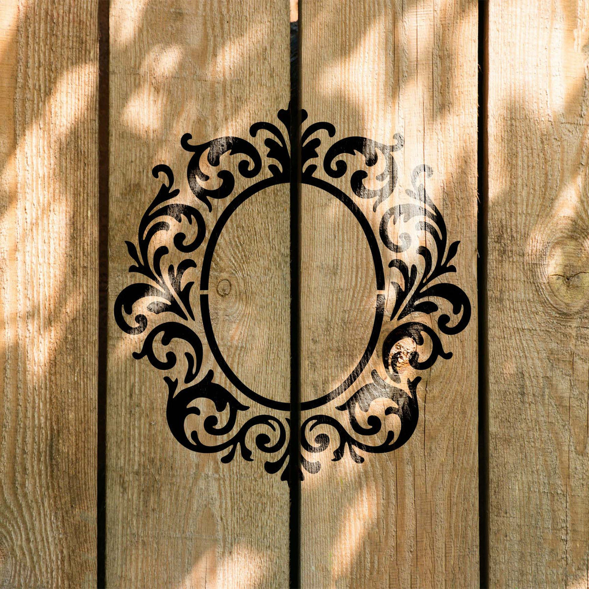 Sunlit wood displays the Ornate Monogram Frame Stencil surrounded by elegant curling flourishes