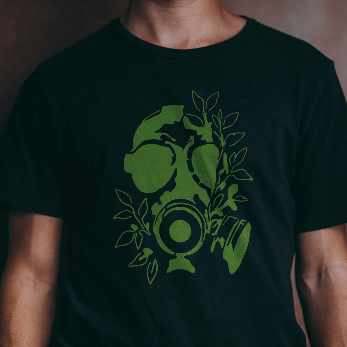 Nature reclaims a gas mask skull in the Overgrown Gas Mask Skull Stencil printed in green on a black shirt