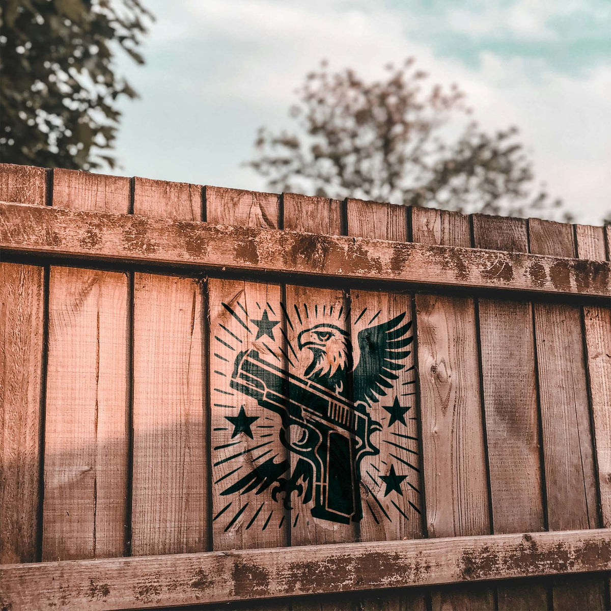 On a rustic wood fence, the Patriotic Eagle and Handgun Stencil features an eagle, pistol, and stars.