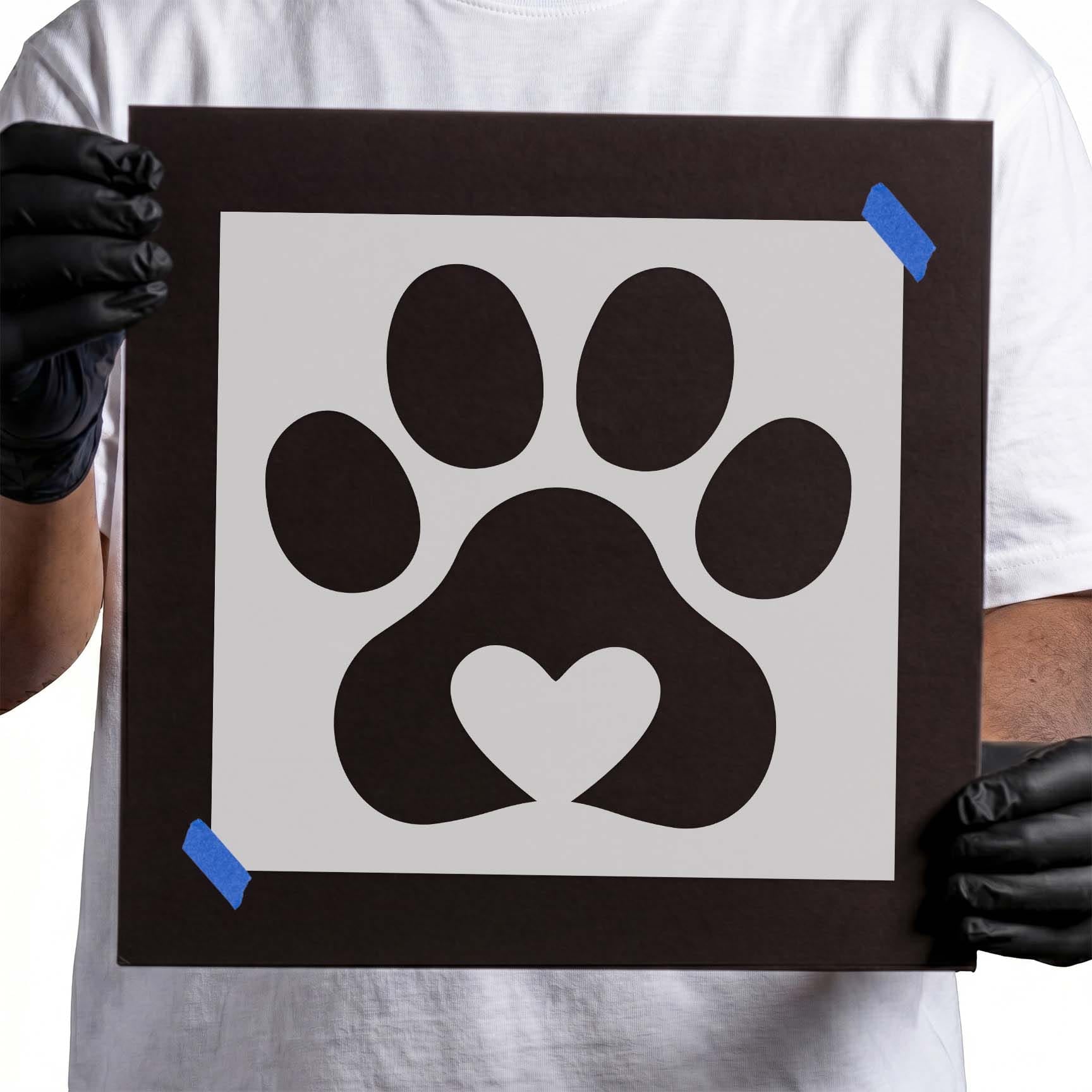 Gloved hands holding Heart Paw Print Stencil taped to cardboard