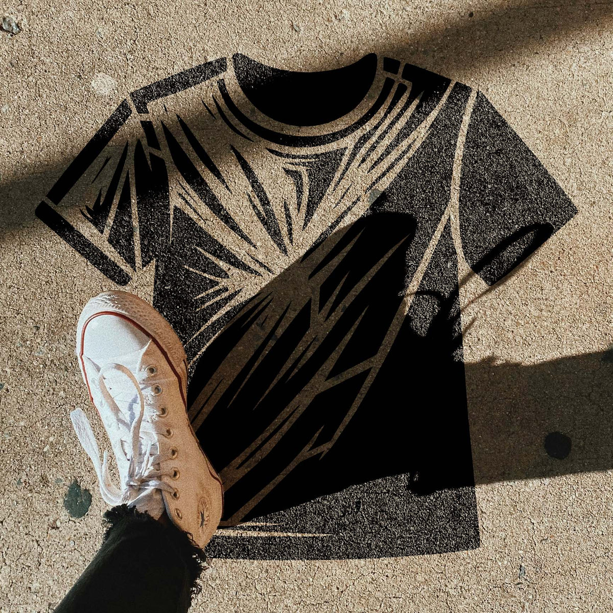 Black Radiant T-Shirt Graphic Stencil appears on pavement beside a white sneaker