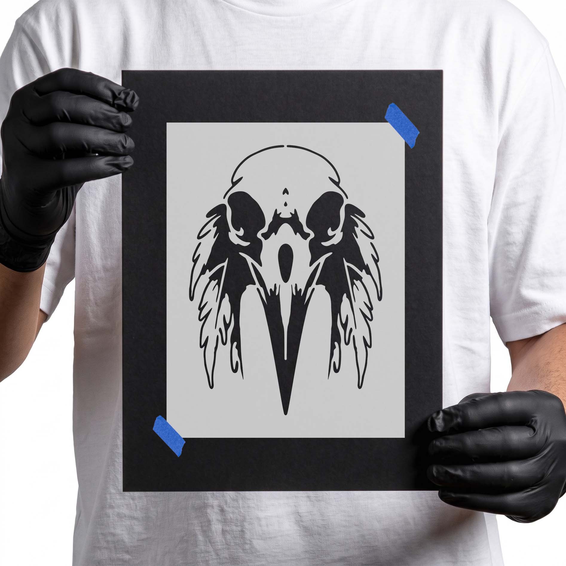 Person holding Feathered Raven Skull Stencil taped to cardboard