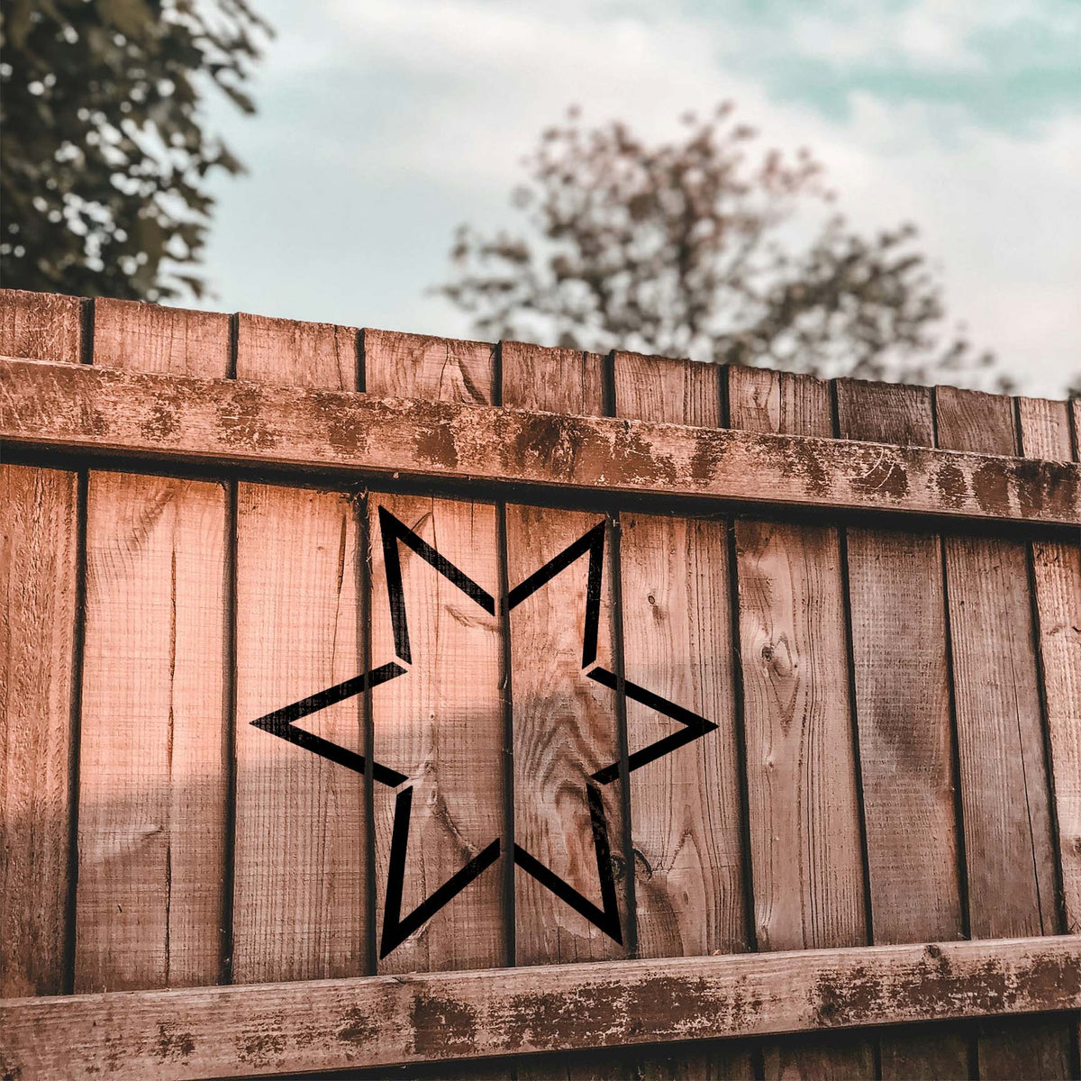 Rustic wood fencing displays the Six Point Star Outline Stencil in a bold black finish