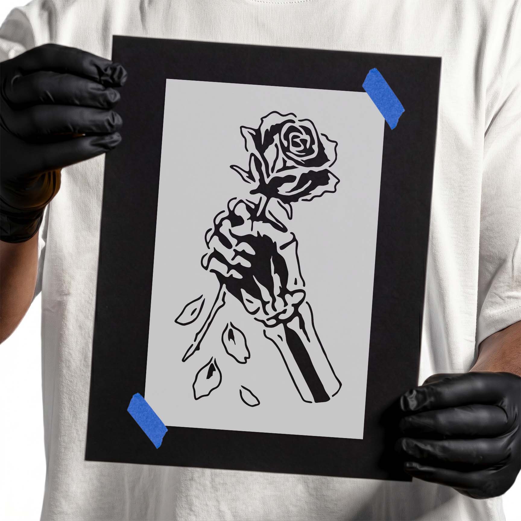 Person holding Skeleton Hand Holding Rose Stencil taped to cardboard