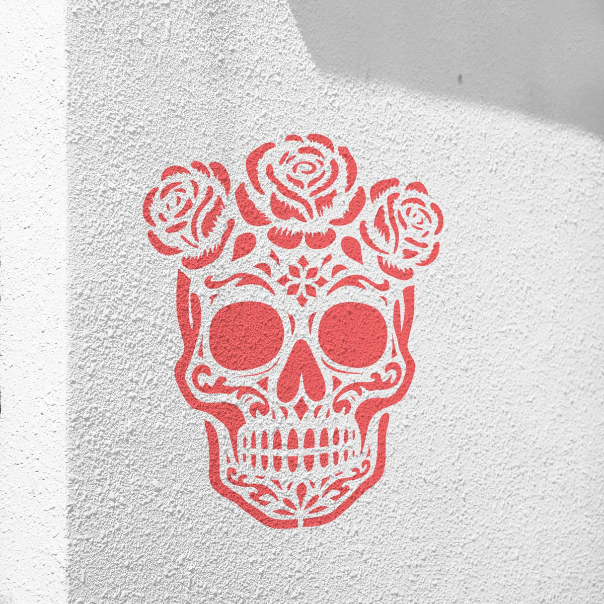 A floral Skull with Roses Stencil in soft pink decorates a textured white stucco wall.