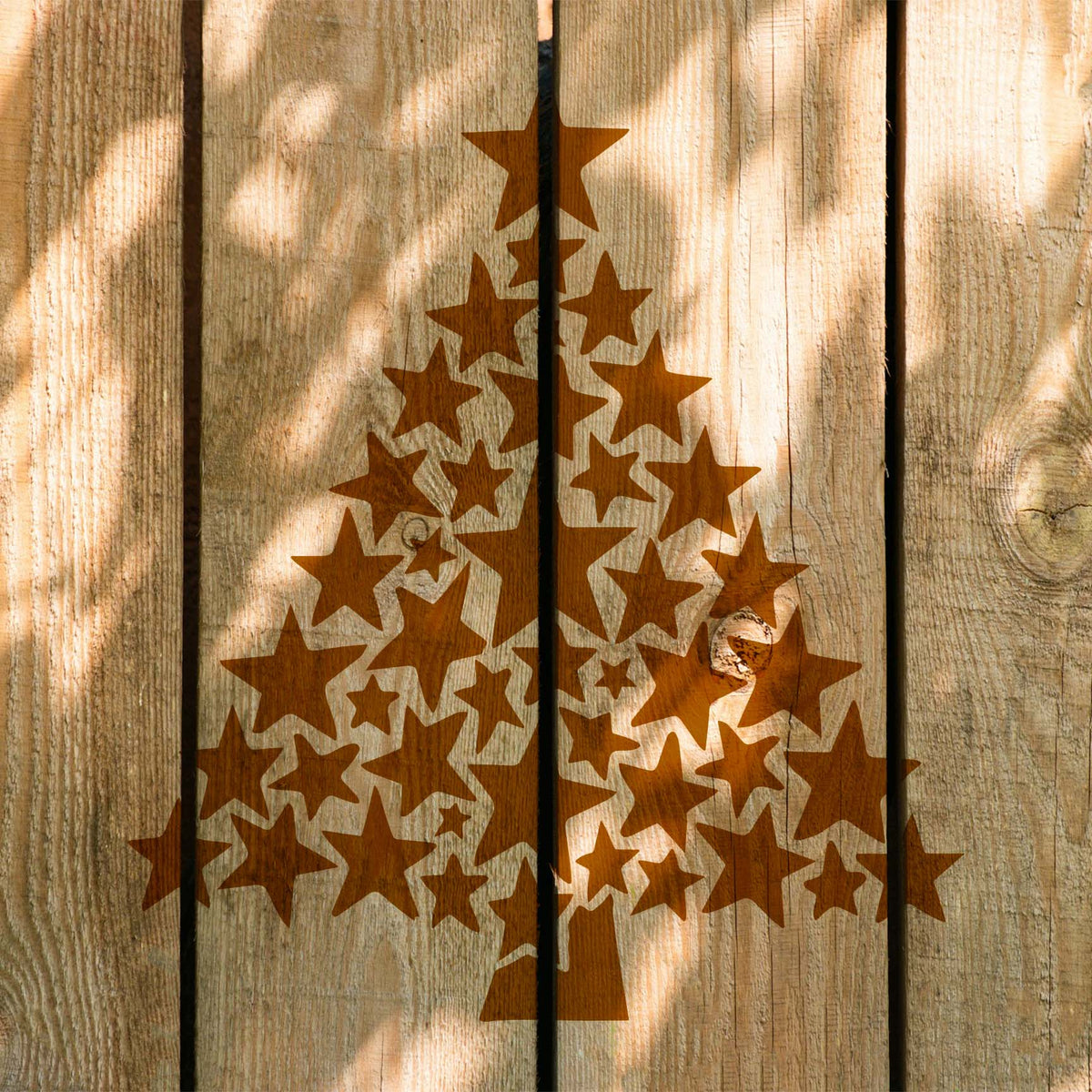 Sunlit fence boards feature the Starry Christmas Tree Stencil in a warm wood-toned finish.