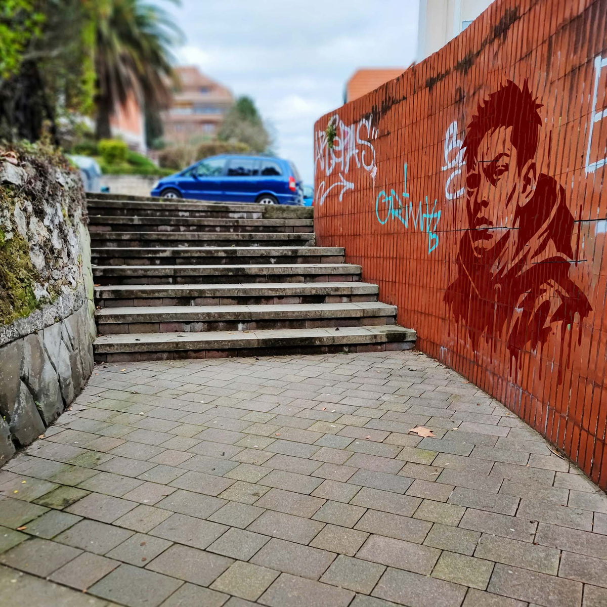 Street Style Portrait Stencil painted in dark red on a graffiti-covered brick wall beside outdoor stairs.