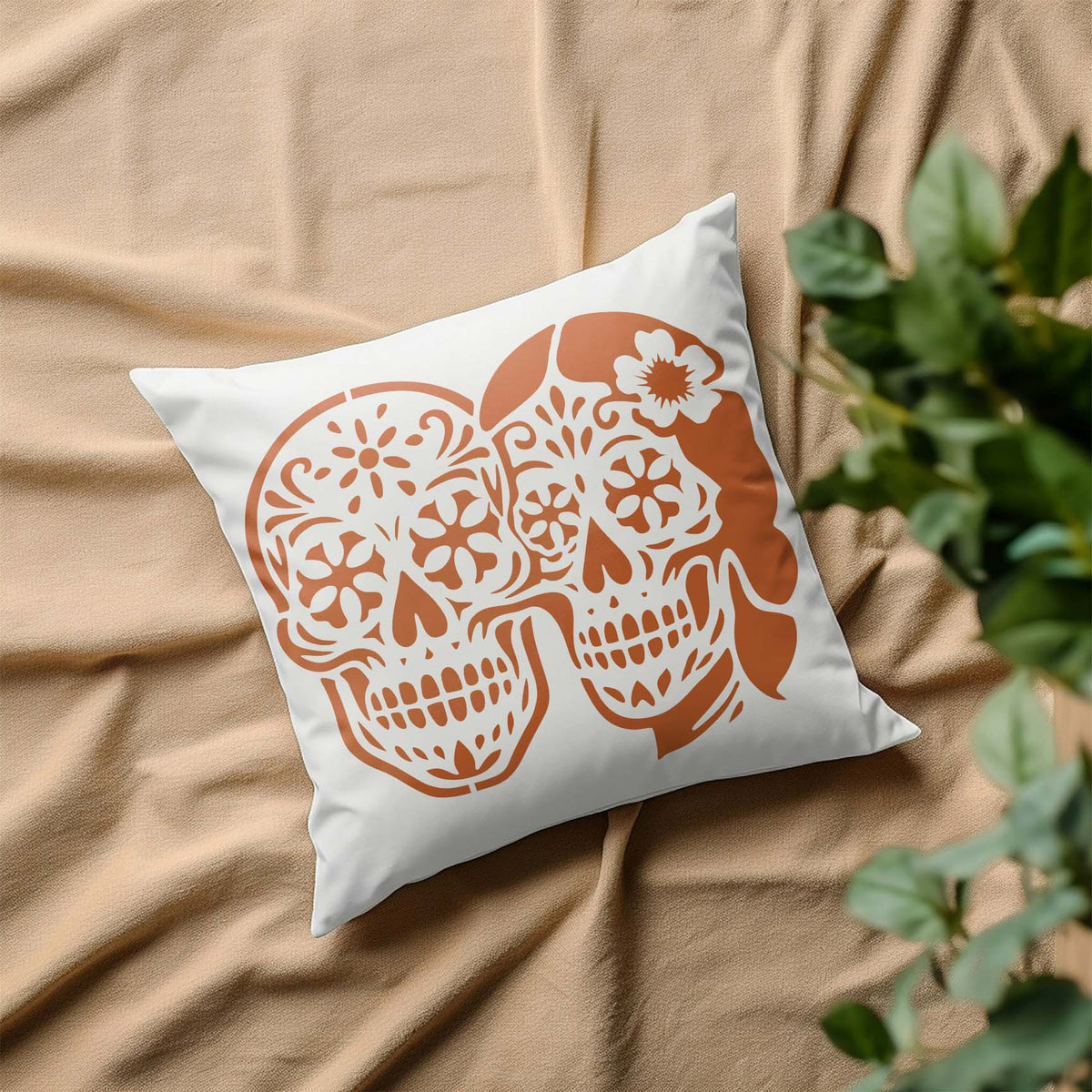Sugar Skull Couple Stencil decorates a white pillow with two ornate skulls and floral details