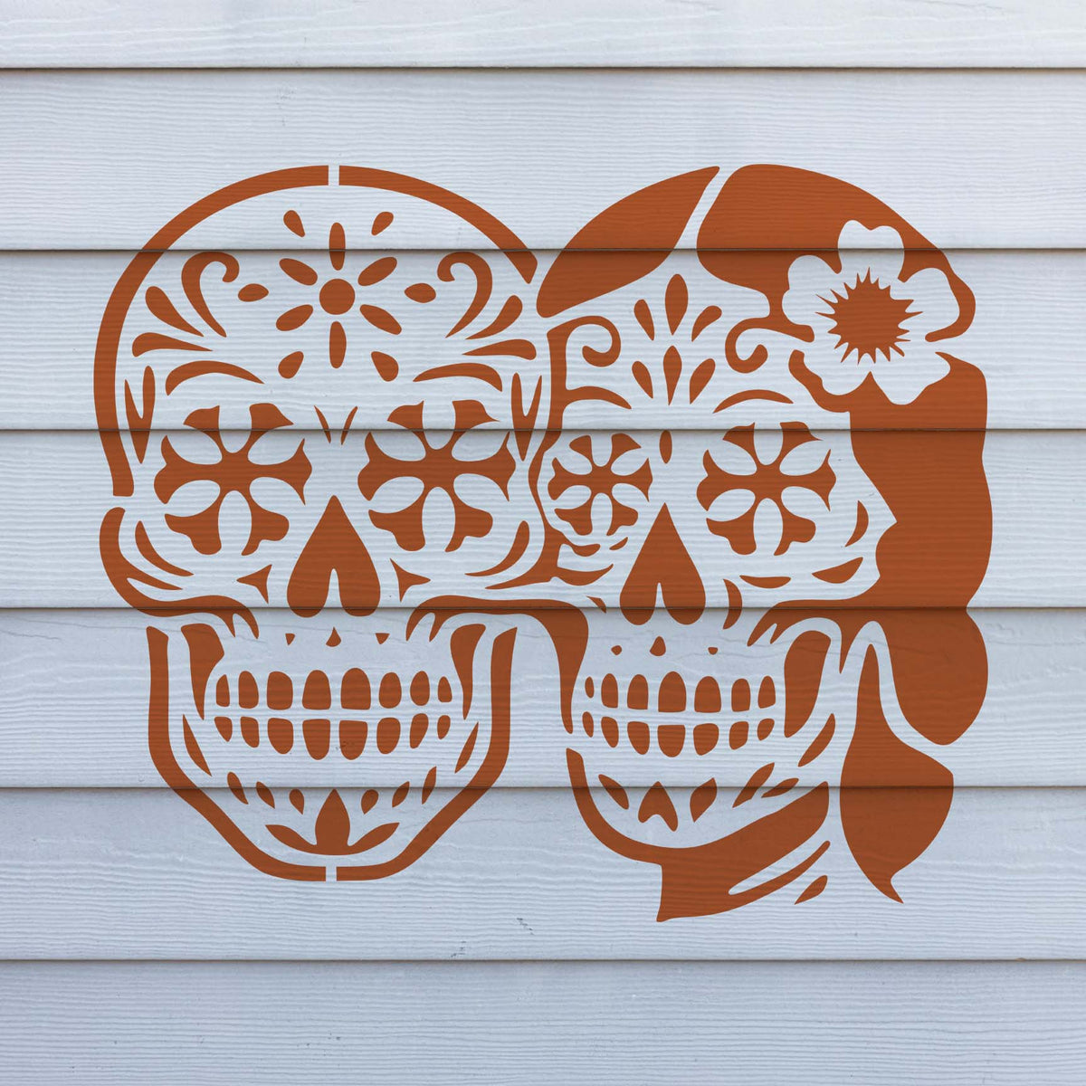 Warm orange Sugar Skull Couple Stencil features two decorated skulls across white exterior siding