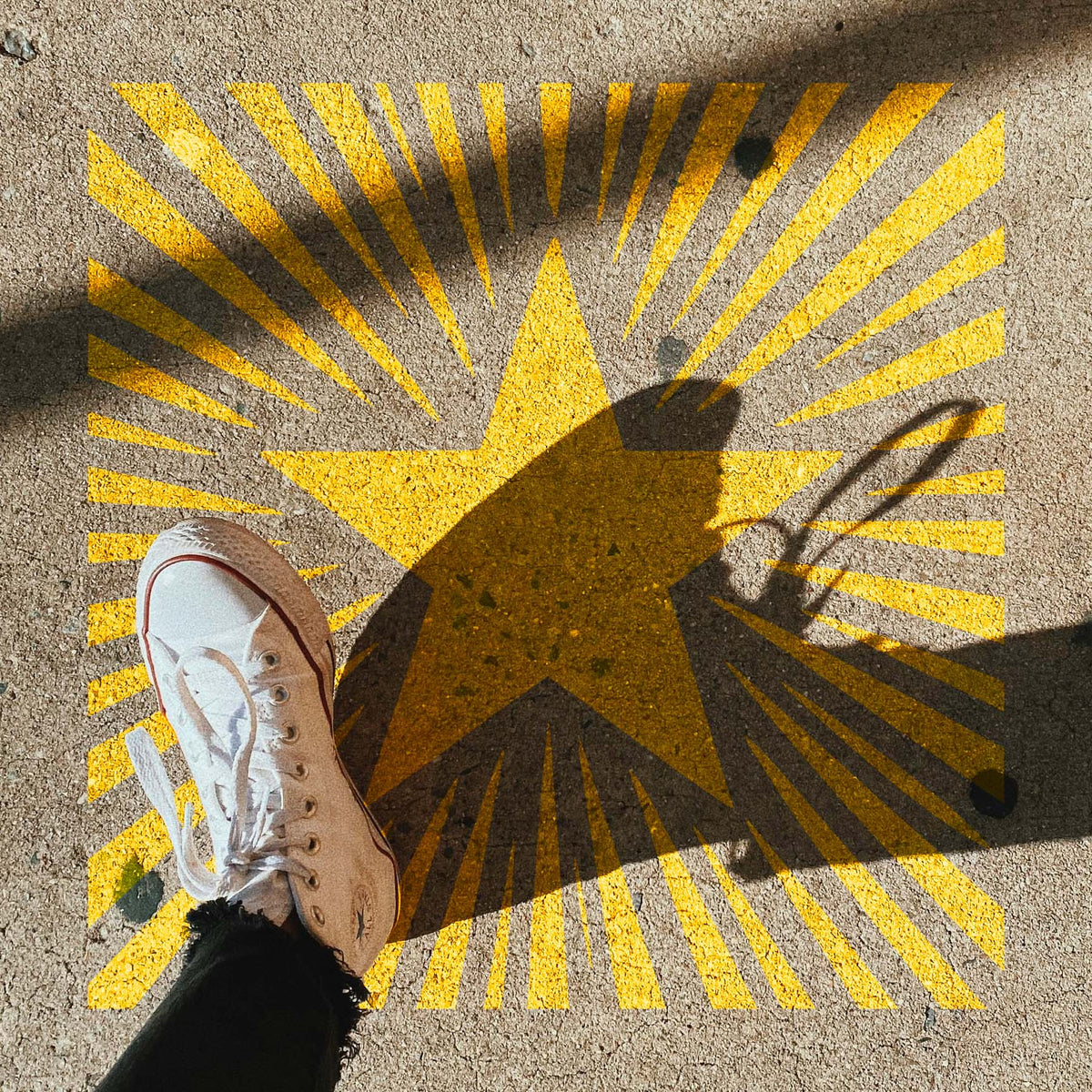 Golden Sunburst Star Stencil shines across a concrete sidewalk beneath dramatic shadows