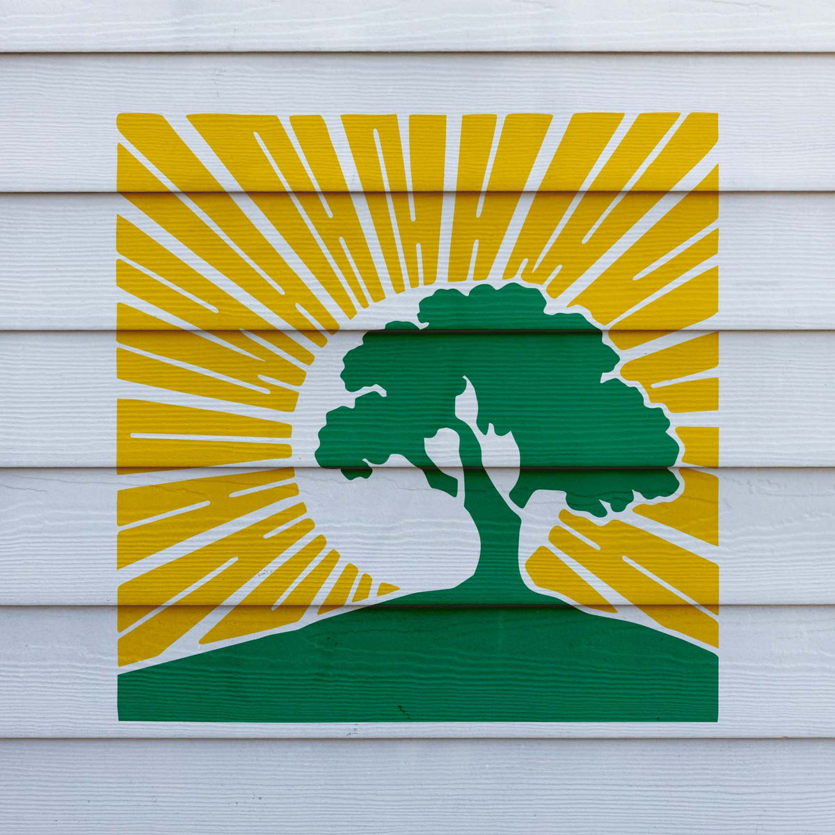 Bright yellow sunbeams surround the green Sunrise Tree Silhouette Stencil painted on white siding