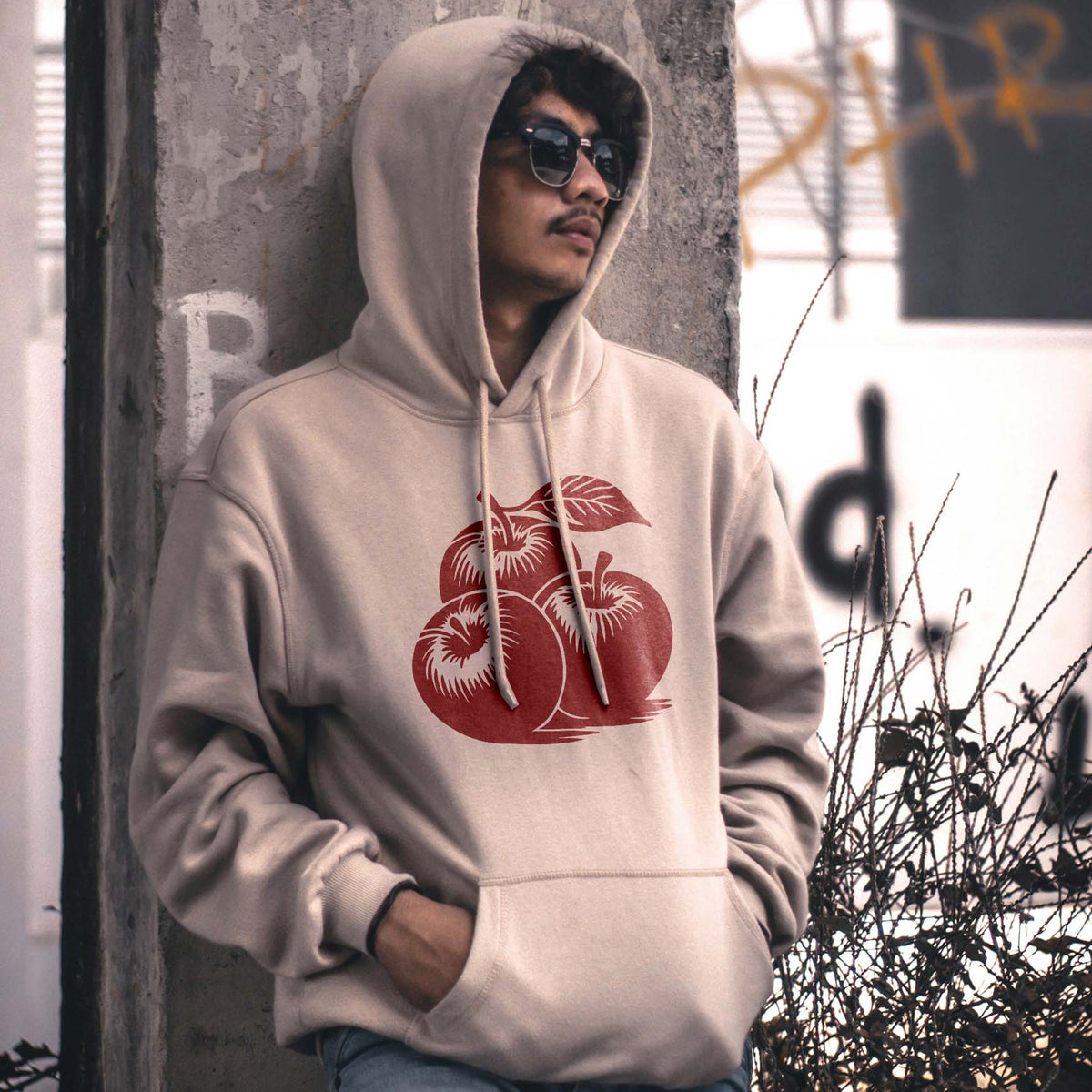 A beige hoodie features the Three Apple Cluster Stencil in muted red across the chest.