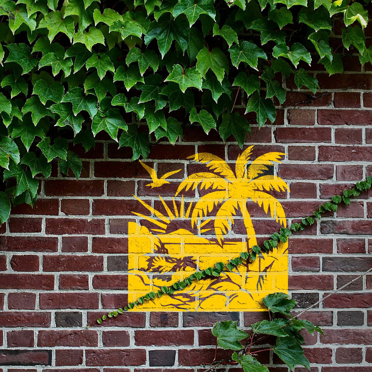 Bright yellow Tropical Beach Sunset Stencil adds palm trees, crashing waves and a bird to an ivy brick wall
