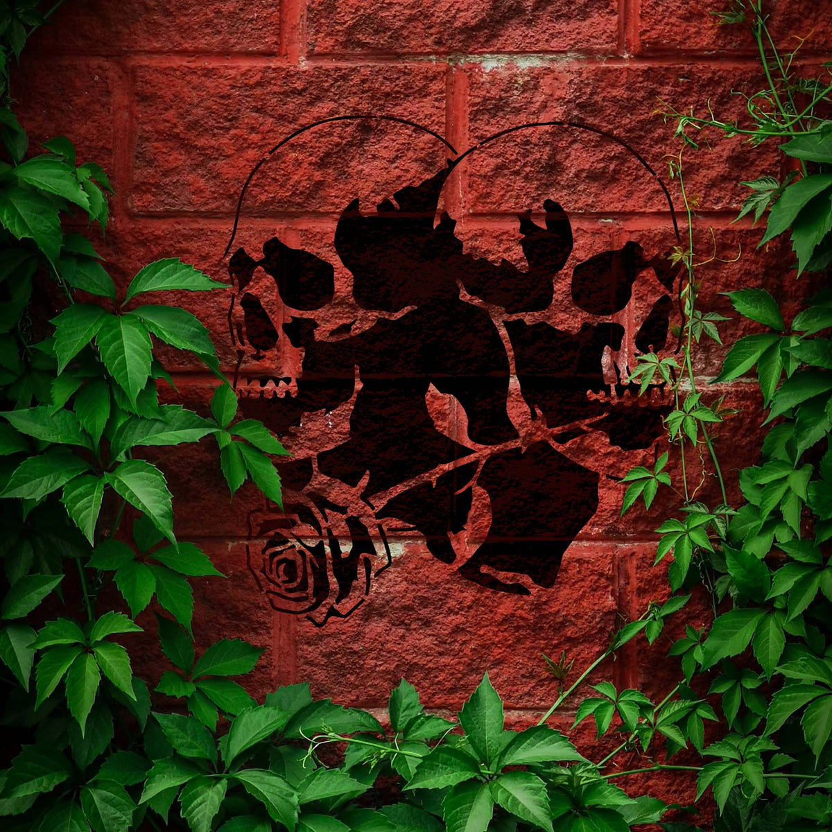 Twin Skull Rose Stencil forms a dark double-skull design with a rose across a leafy red brick wall