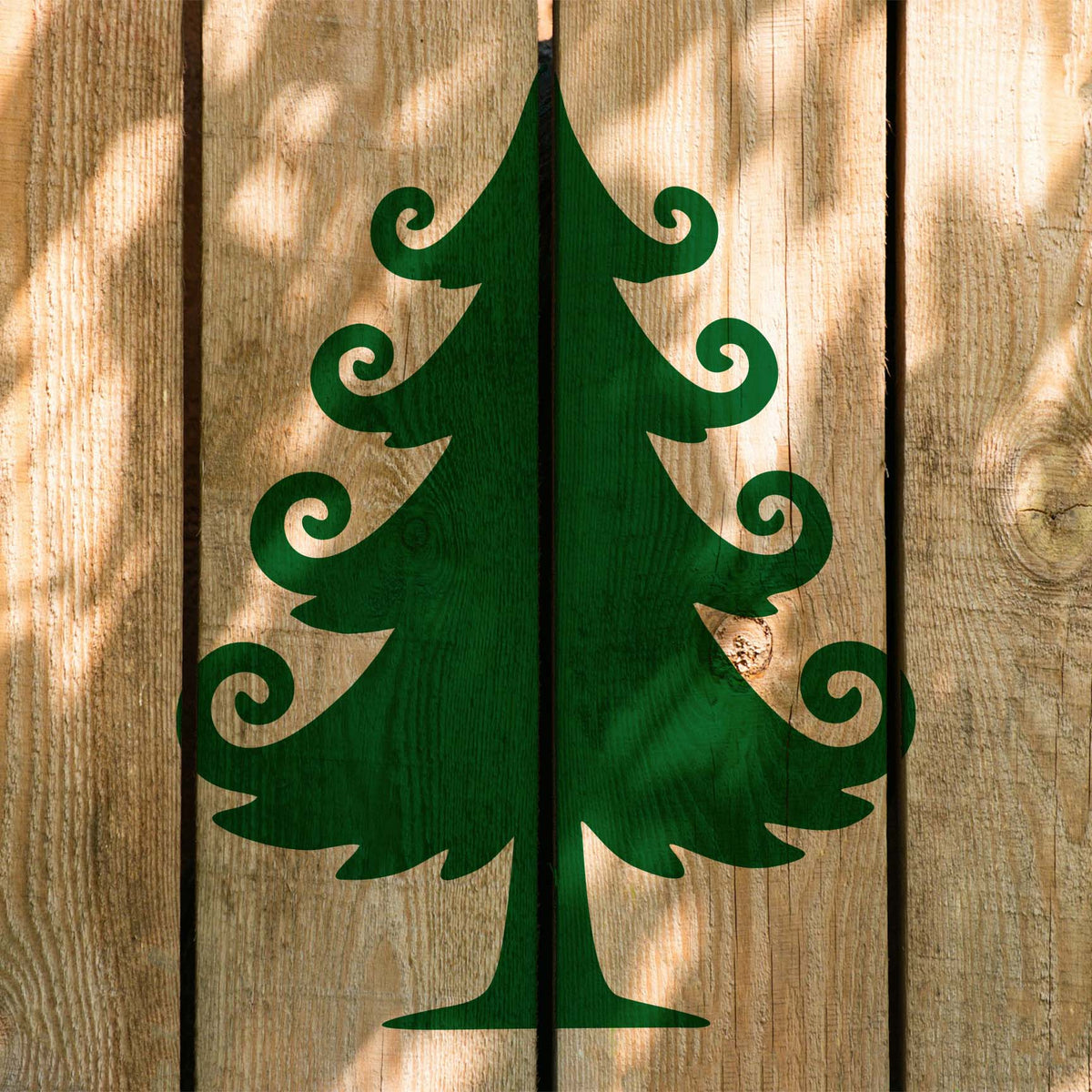 Whimsical Christmas Tree Stencil shown in green across sunlit vertical wooden fence boards.