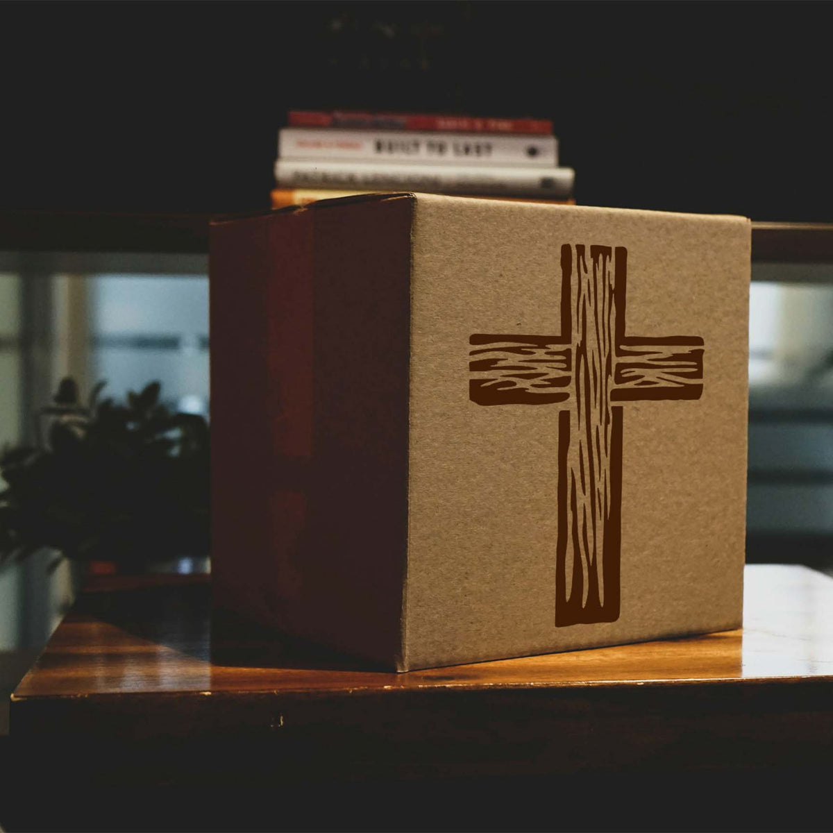 Wooden Christian Cross Stencil printed on a cardboard box beside stacked books on a table