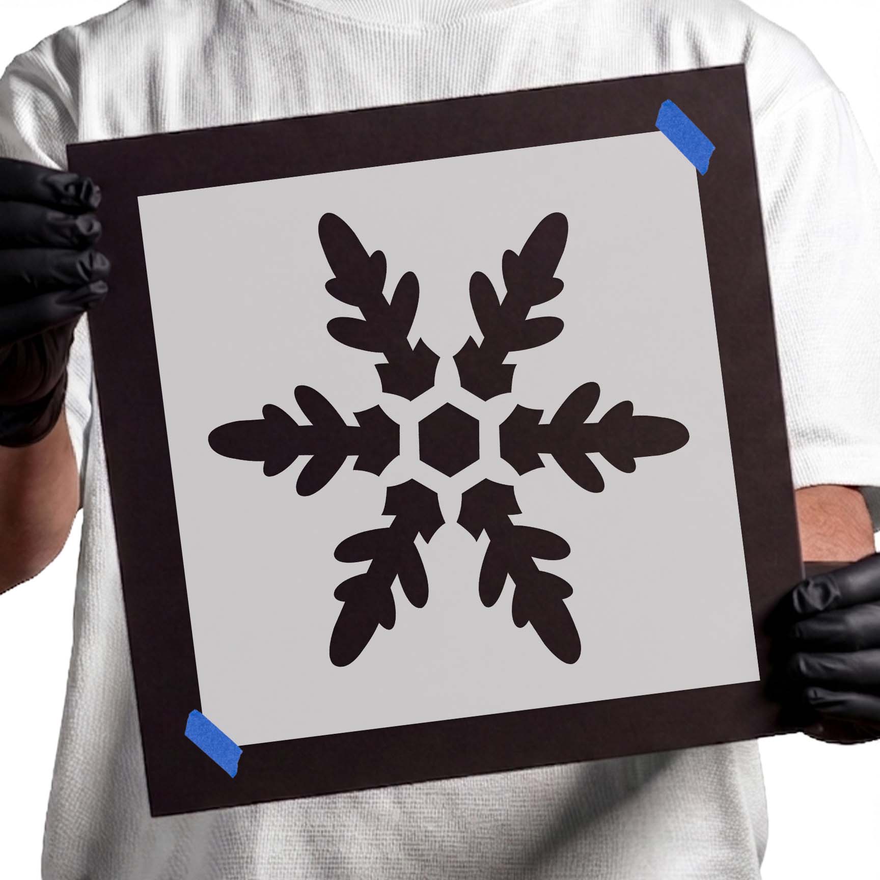 Person holding reusable Snowflake Stencil taped to cardboard