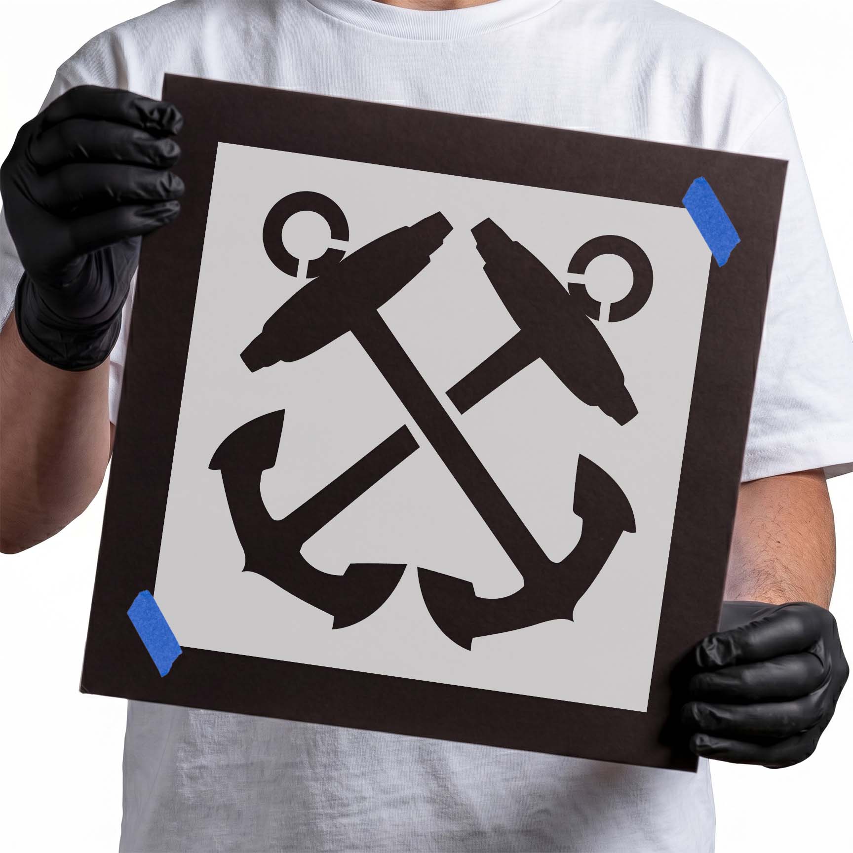 Gloved hands holding Mylar Crossed Anchors Stencil taped to cardboard