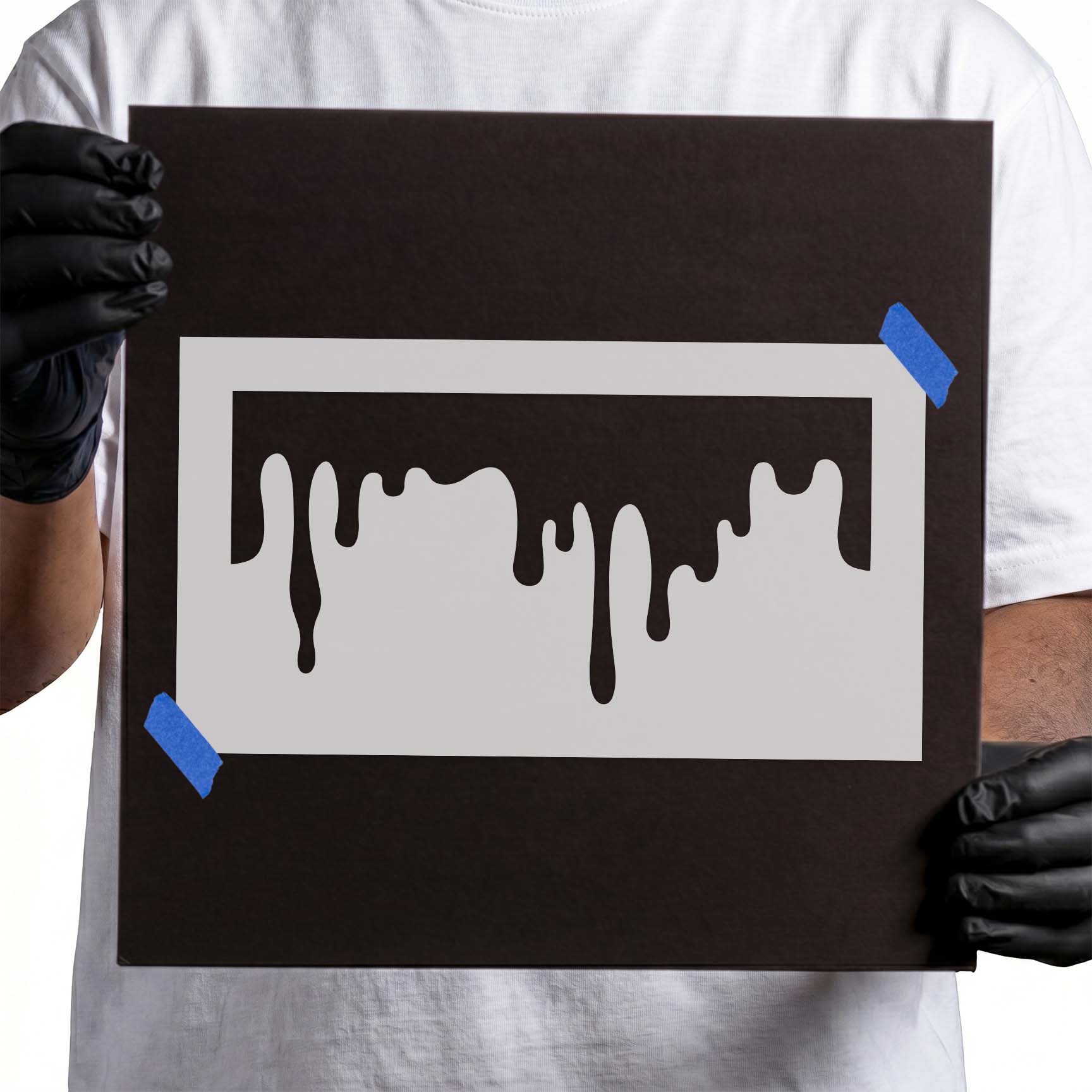 Person holding a laser-cut Dripping Paint Stencil taped to cardboard