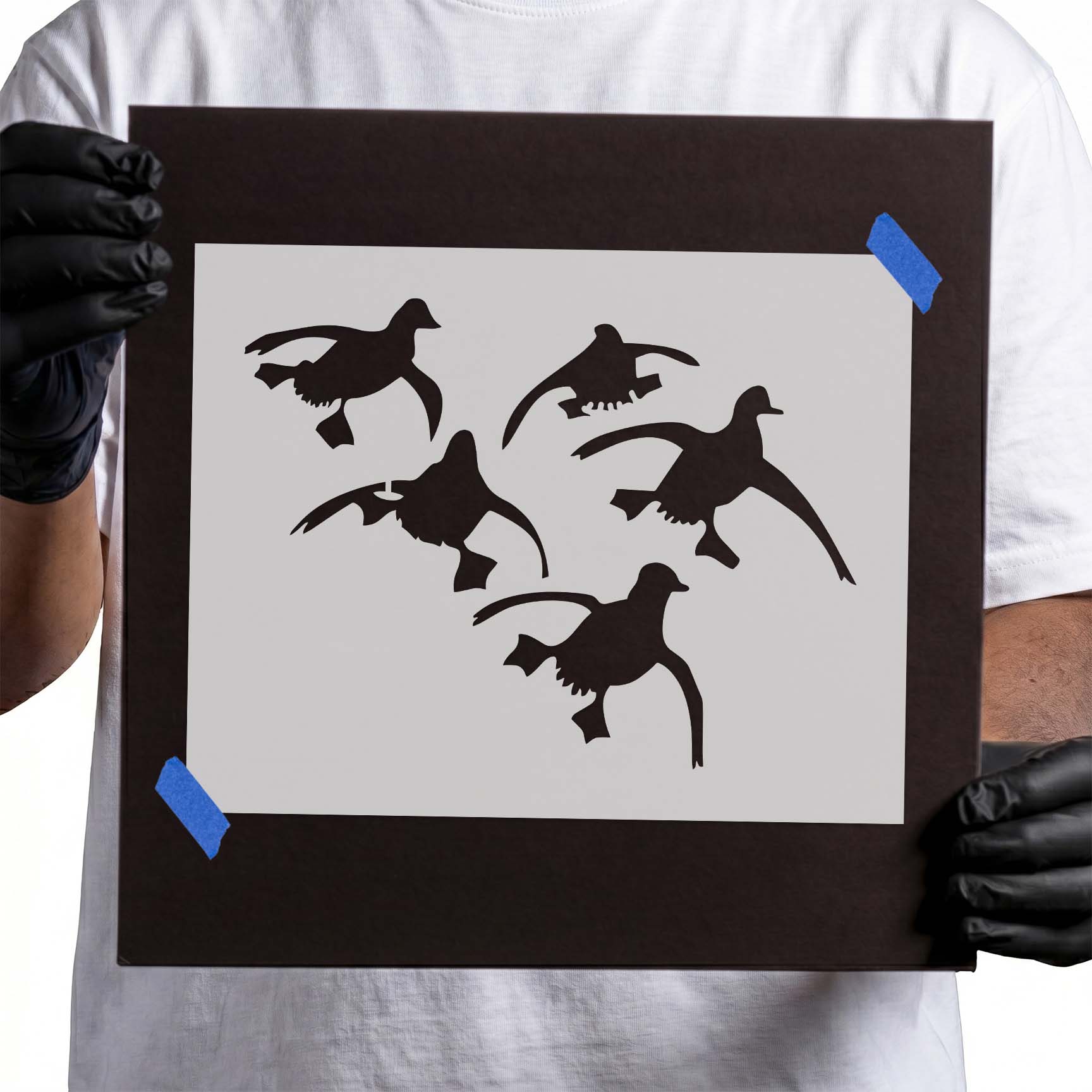 Person holding flying ducks stencil with four duck silhouettes.