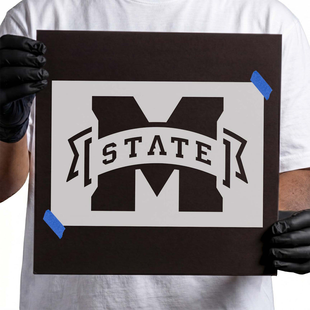 Person holding Mississippi State Bulldogs M State white Mylar stencil on black backing