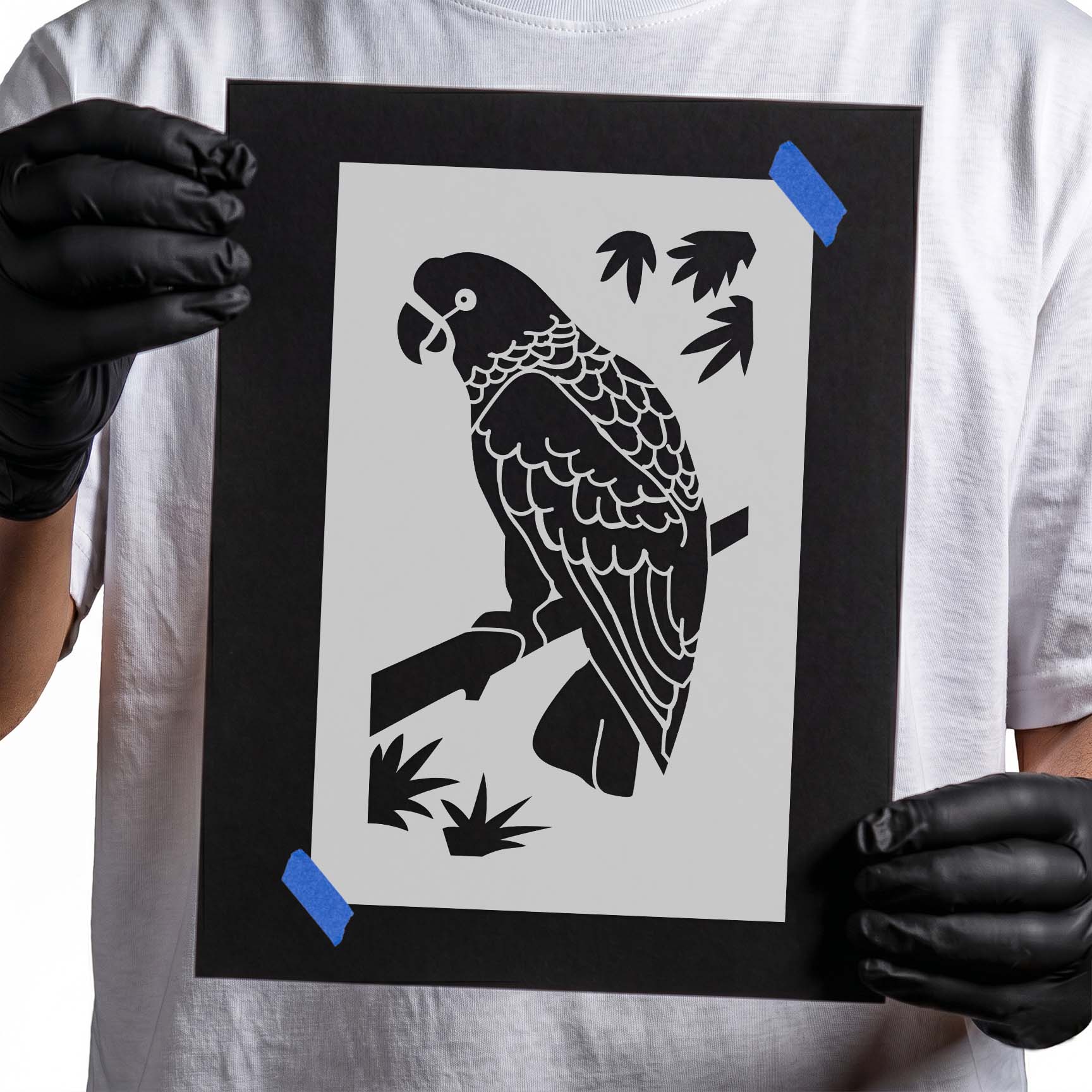 Person holding laser-cut parrot stencil perched on tree branch.