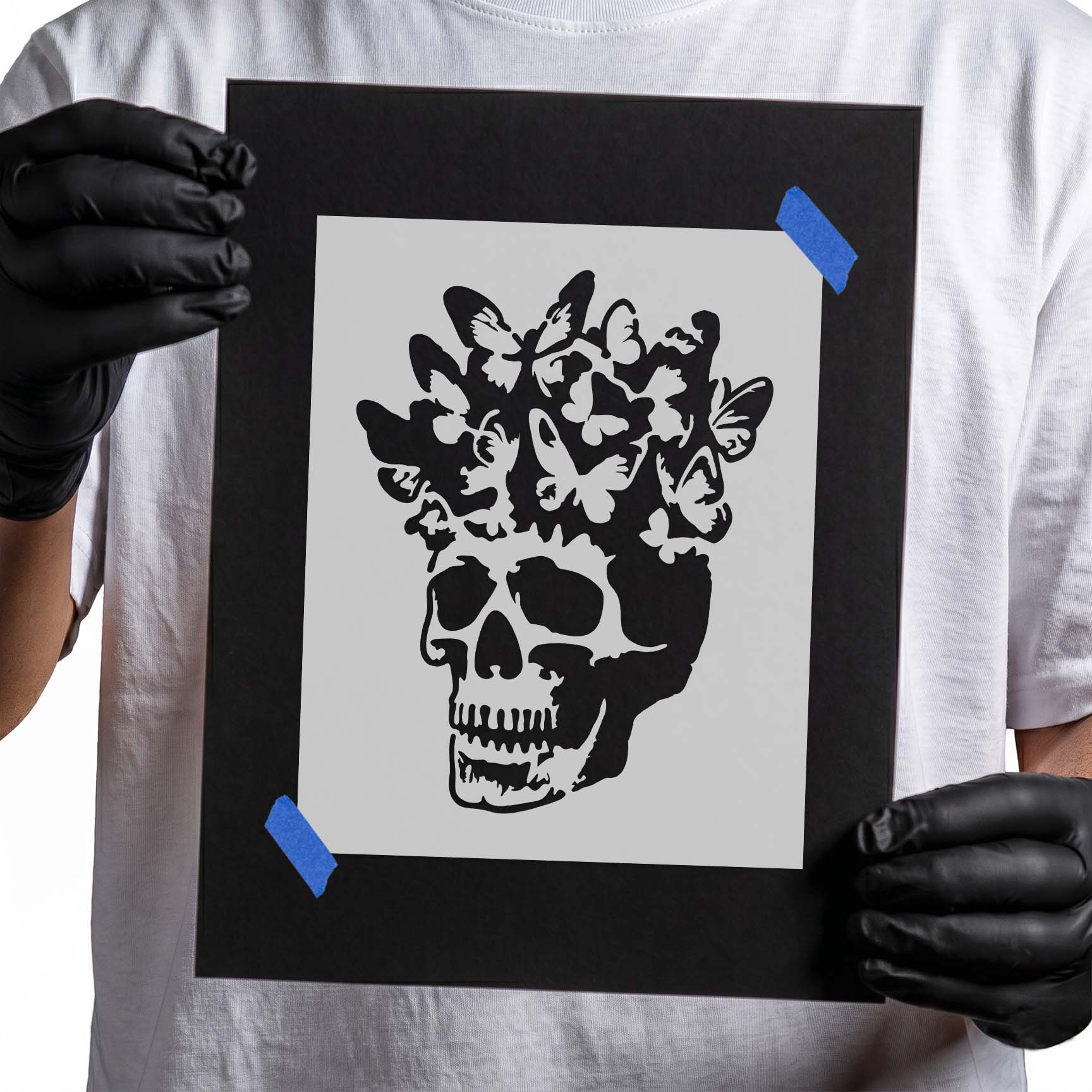 Gloved hands holding Butterfly Bloom Skull Stencil taped to black cardboard