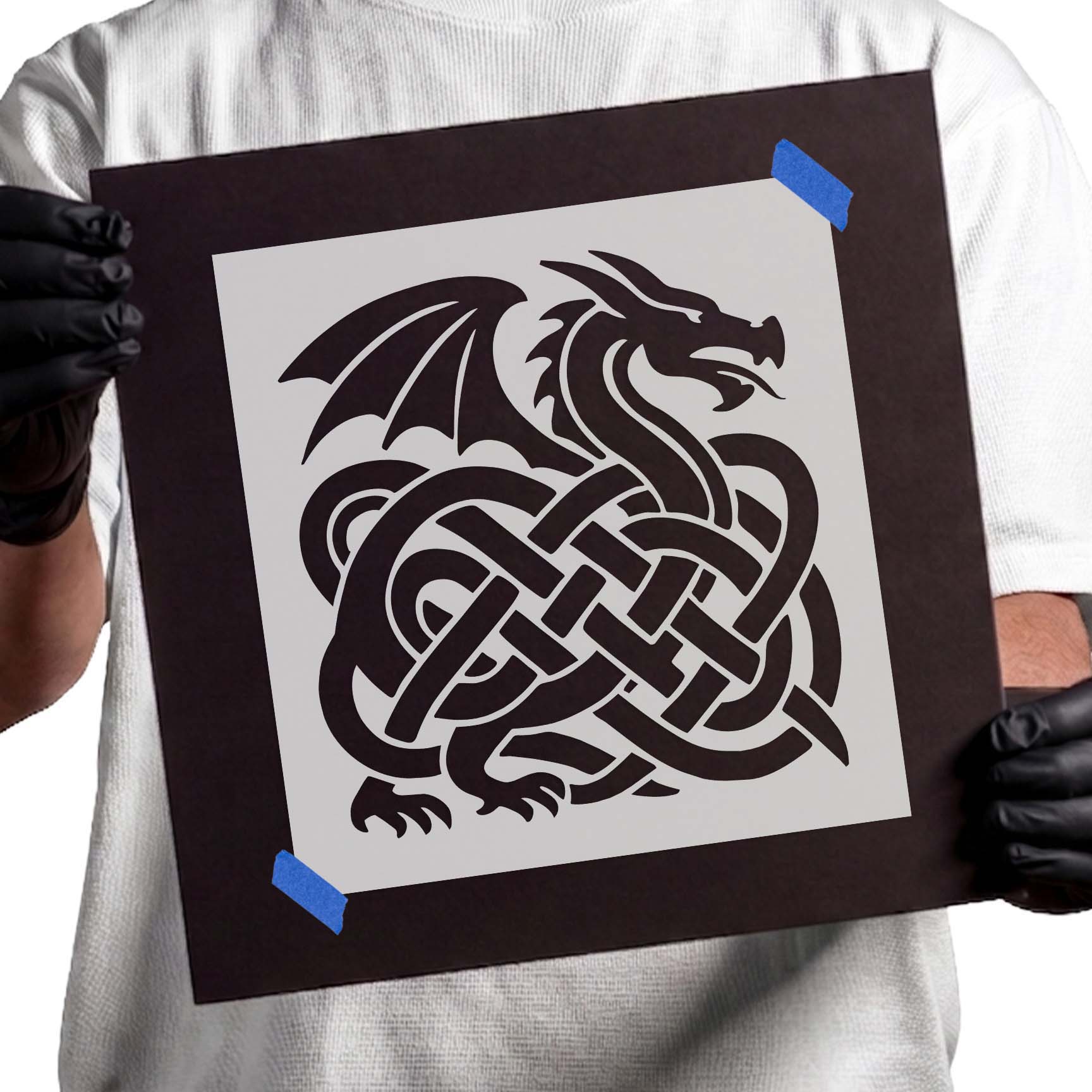 Gloved hands holding Celtic Dragon Knot Stencil taped to black cardboard